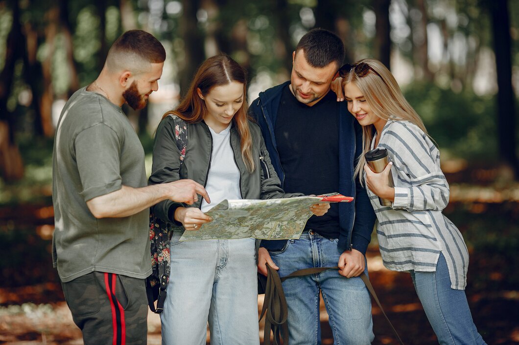 A group of four people studies a map together in a sunlit forest, surrounded by trees and earthy scenery.