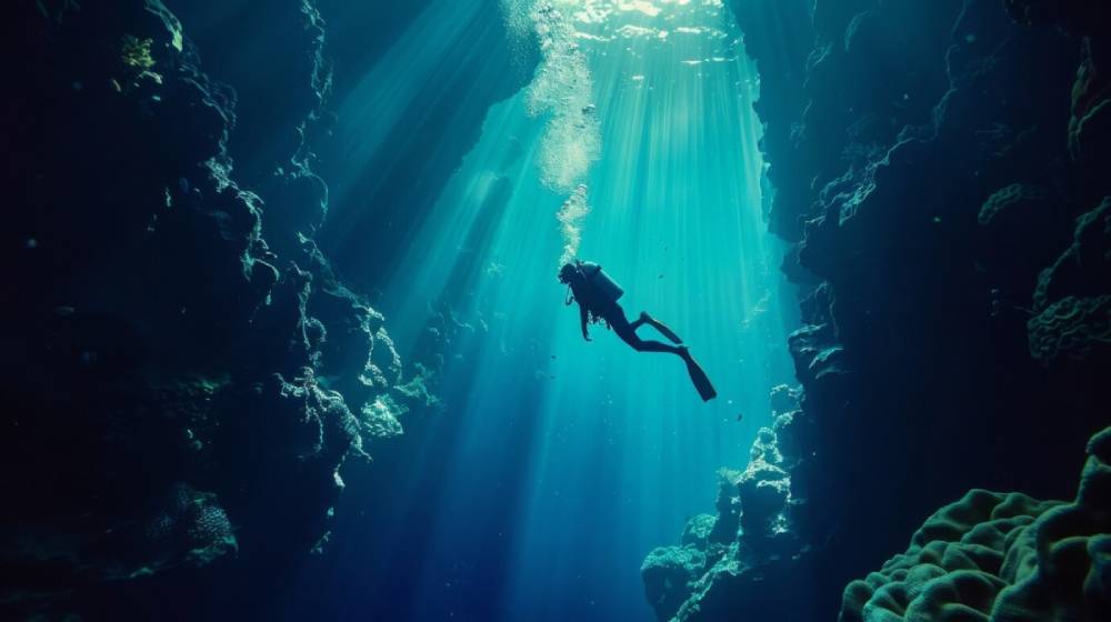 A diver glides through a sunlit underwater canyon, surrounded by vibrant coral formations and shafts of shimmering light.