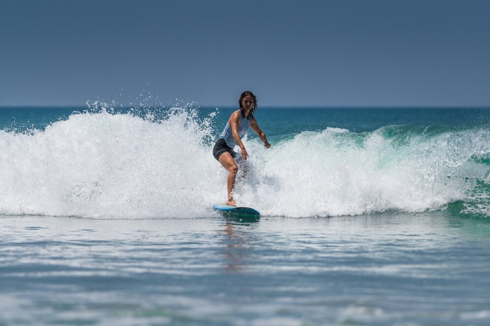 A surfer riding a wave on a sunny day, with turquoise water and white foam splashing around the board.