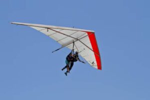 A tandem hang glider with two people soaring against a clear blue sky, showcasing a white wing with red highlights.