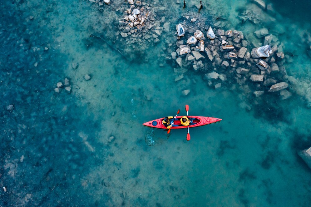 Aerial view of two people kayaking in clear turquoise water surrounded by rocky shores.