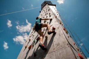 A climber ascends a tall rock wall under a bright blue sky, showcasing athleticism and outdoor adventure.