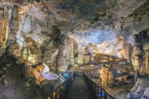 A scenic view of a cave featuring intricate stalactites and stalagmites, with a wooden walkway leading through the illuminated space.