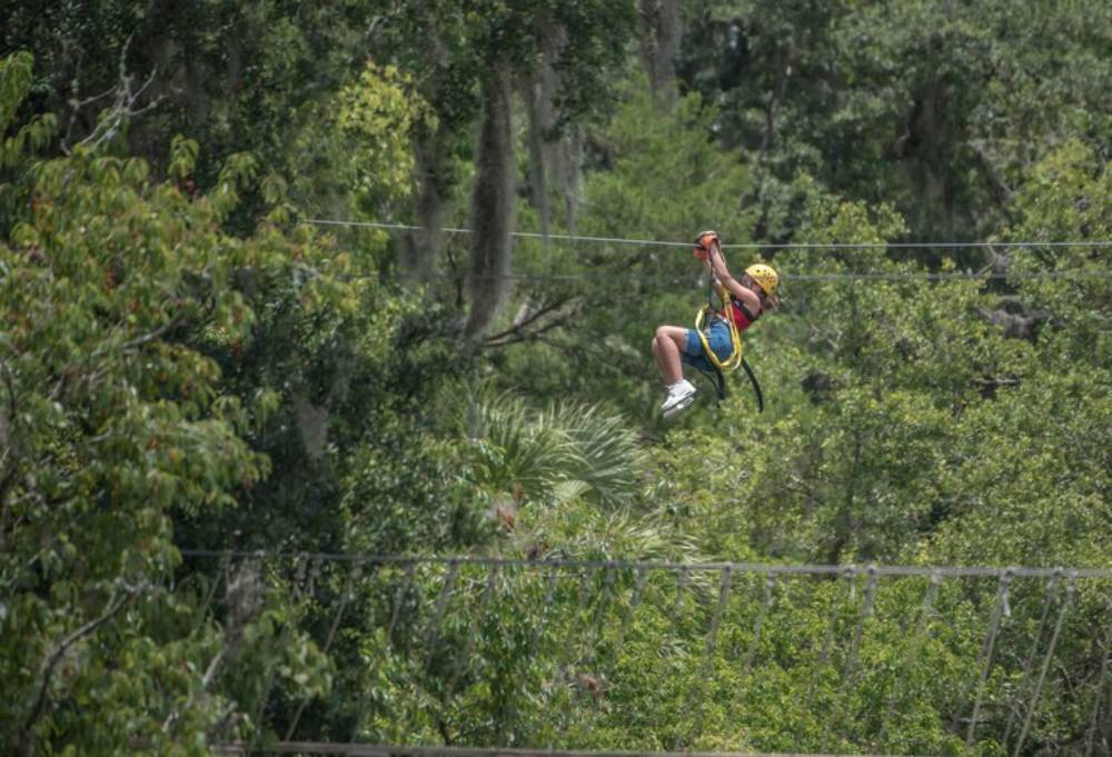 A child in a yellow helmet zip lines through lush green trees, enjoying a thrilling outdoor adventure.
